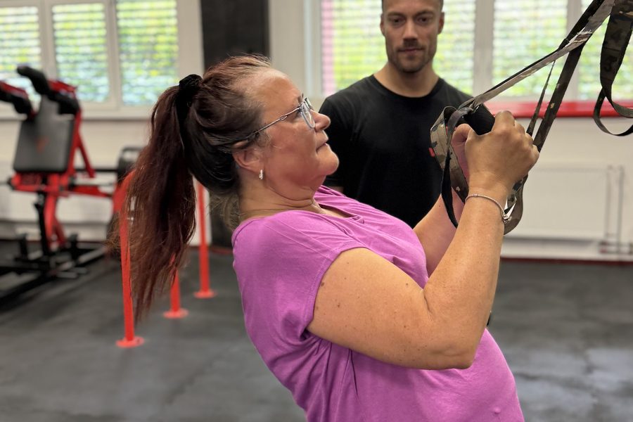 Klientka po čtyřicítce cvičí na TRX pod vedením trenéra