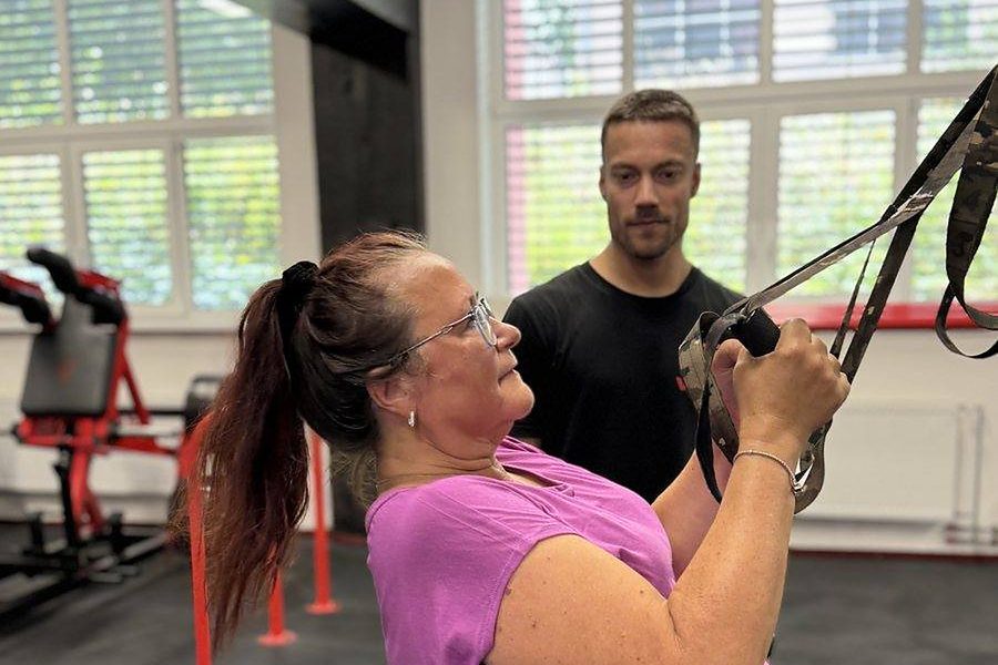 Trenér FitWay40 dohlíží na klientku při cviku s posilovacími popruhy