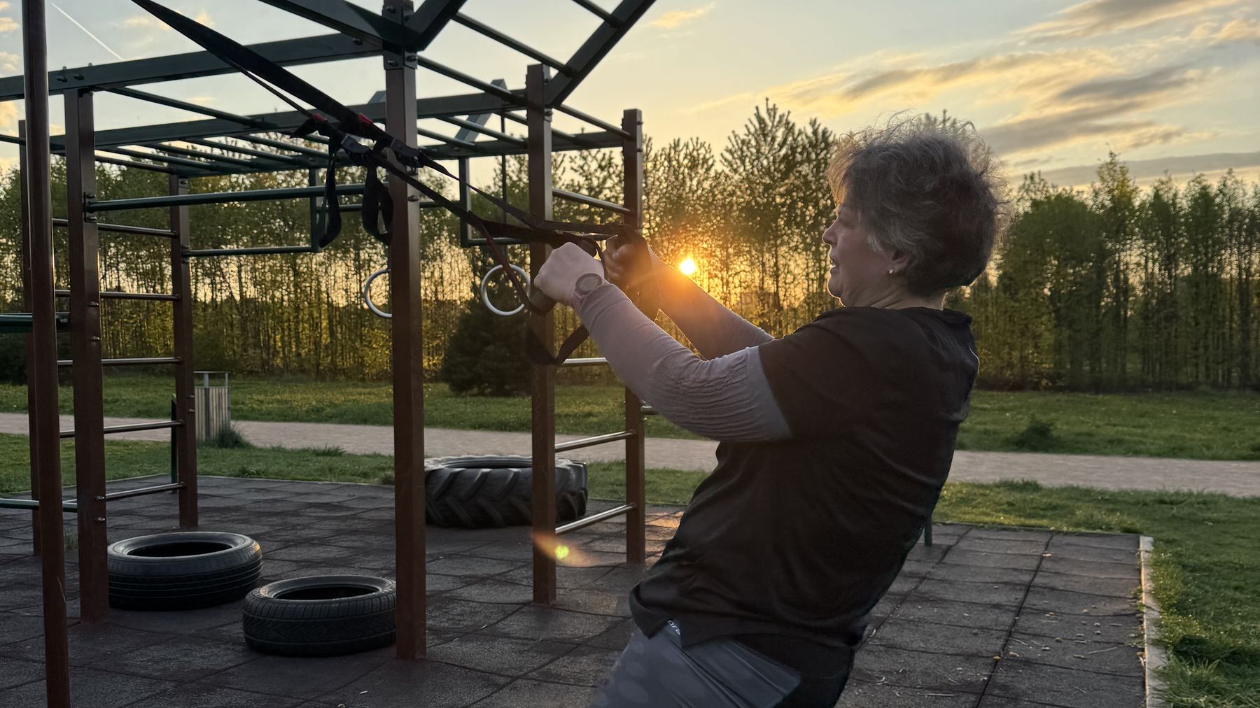 Klientka FitWay40 cvičí na TRX na workoutovém hřišti při západu slunce