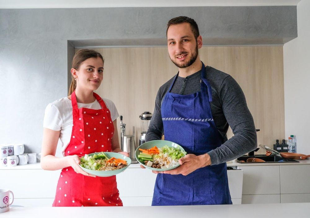 Láďa a Tina drží talíře s hotovým jídlem v kuchyni